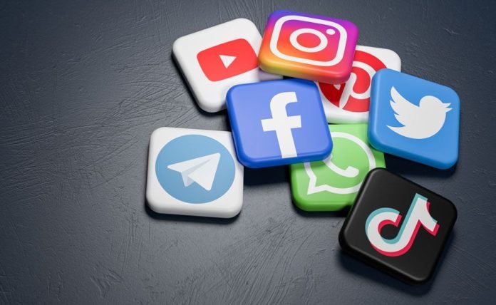 Logos of the major social media and messaging sites (Youtube, Instagram, Pinterest, Twitter, Facebook, Whatsapp, Telegram, Tiktok) on a heap on a dark table. Copy space - Web banner size